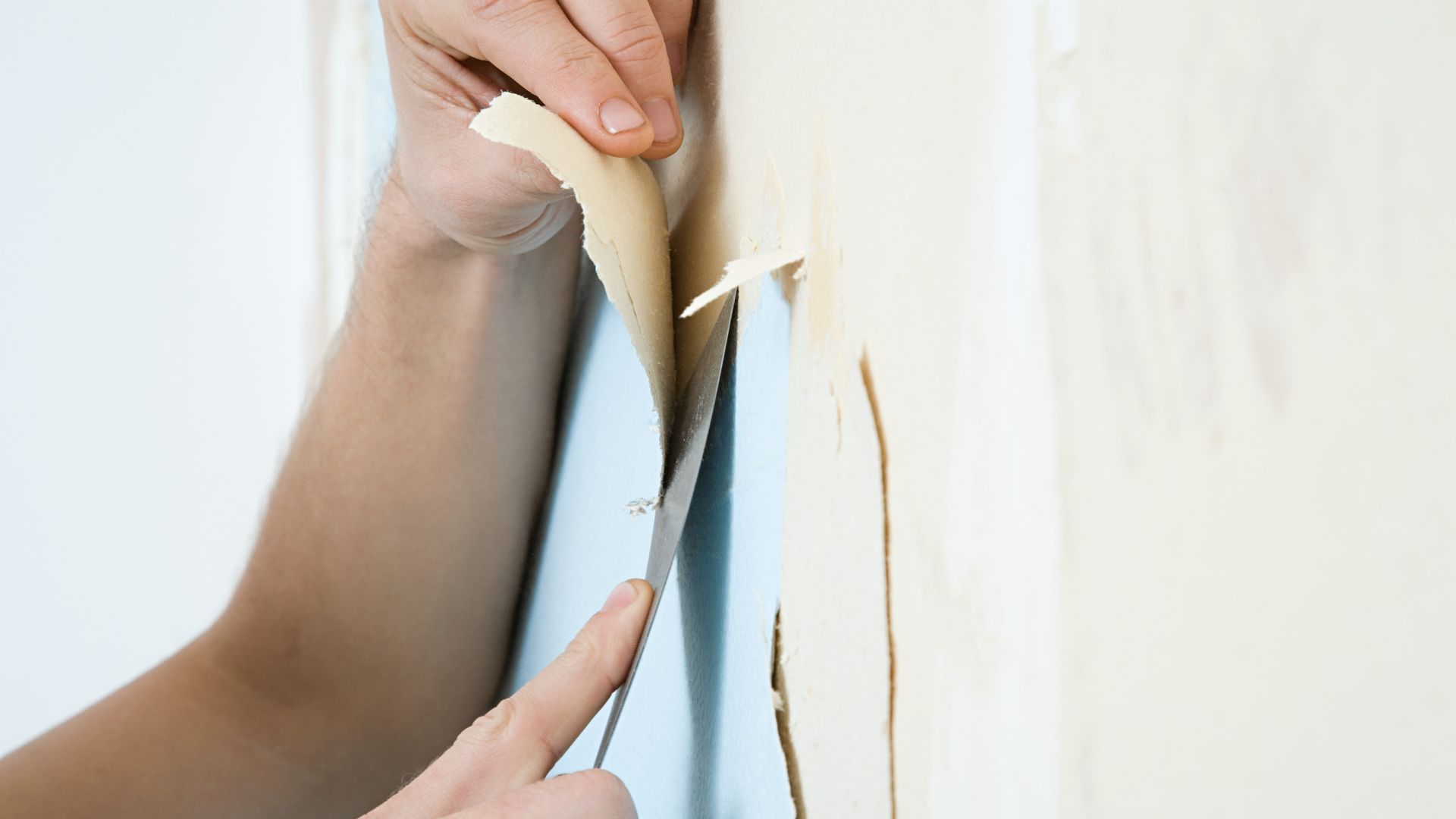 close up of a person scraping pale wallpaper