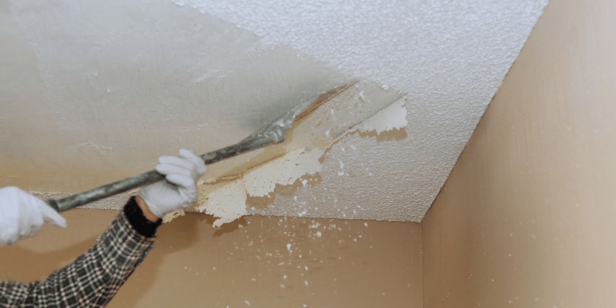 closeup of hands holding a scraper and removing a layer of popcorn texture ceiling